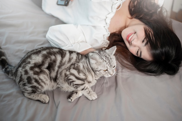 美しいアジアの猫の恋人の女性は彼女の部屋で猫と遊んでいます