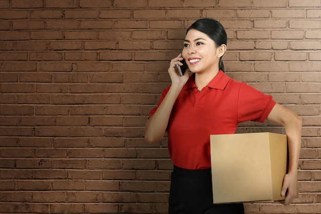 Beautiful asian delivery woman using mobile phone while bring the package