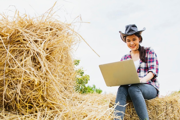 아름다운 아시아 농부 사업가가 들판에 있는 온라인 농업용 타자 노트북에 앉아 있습니다.