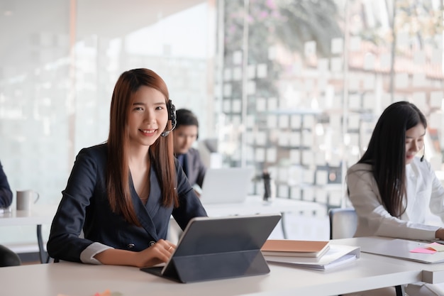 Beautiful asian female call center agent in headset consulting client.