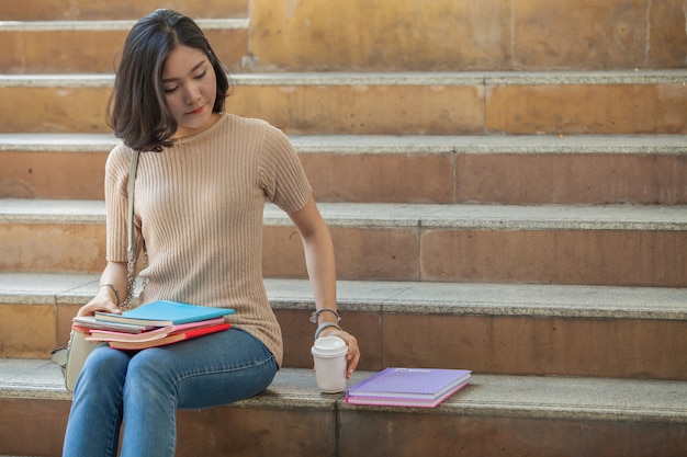 Bello studente di college femminile asiatico che tiene i suoi libri e una tazza di caffè