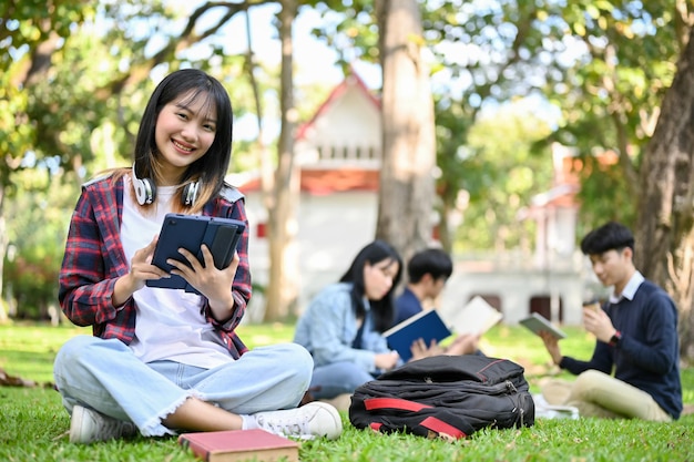 캠퍼스 공원에 앉아 태블릿을 사용하는 아름다운 아시아 여대생