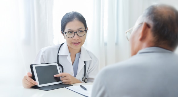 Beautiful Asian Female Doctor giving some information about virus to elderly patient with digital tablet.