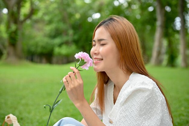 花の匂いを嗅ぐ彼女の手でピンクの花を賞賛する庭の美しいアジアの女性