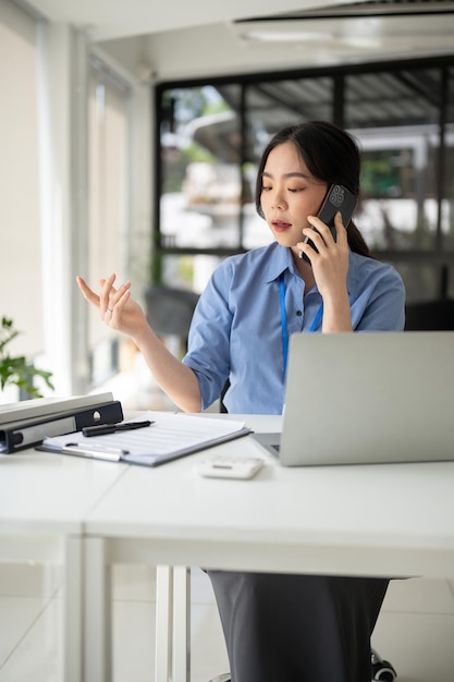 美しいアジア人の女性会社員が机に座りながら電話で商談をしている