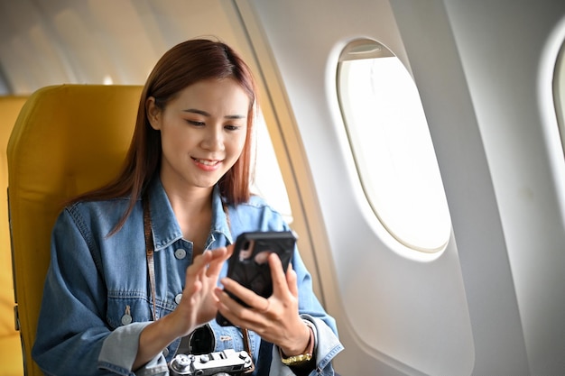 Beautiful asian female passenger sits at the window seat using smartphone during flight