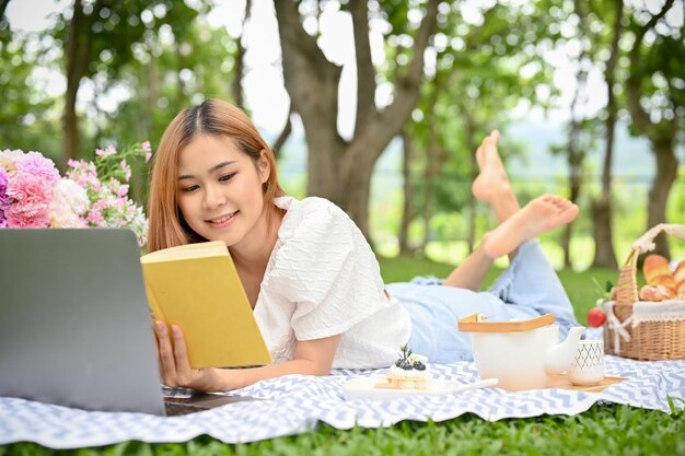 Beautiful Asian female picnicking in the beautiful park relaxes reading her favourite novel