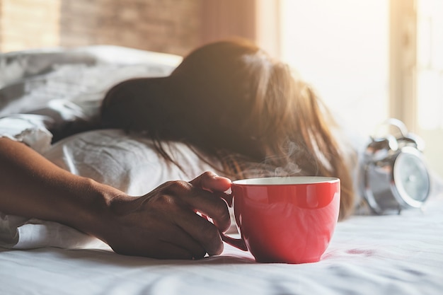 Beautiful asian female sitting in the bed with a cup of coffee. 