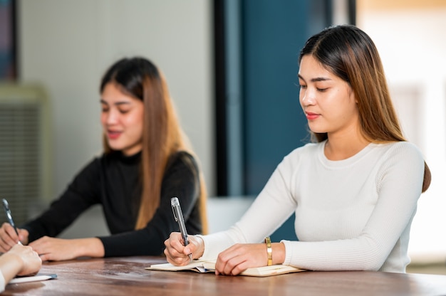 La bella studentessa asiatica si siede per l'esame agli studenti dell'aula universitaria che si siedono nel college universitario di stile di vita di istruzione di fila