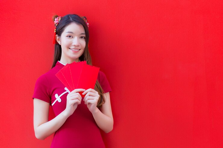 Photo beautiful asian female wears a red cheongsam and holds red envelopes with the red background