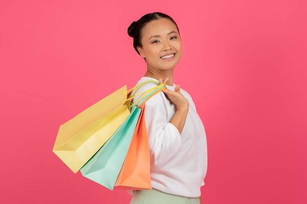 Photo beautiful asian female with shopping bags in hand posing on pink background