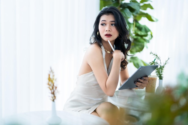 美しいアジアのフリーランスの成功した人々 ビジネス女性ファッション モデル夏白いノースリーブ ドレス インターネット チャットや喫茶店でブログを閲覧するタブレットを使用してカジュアルな作業を使用して