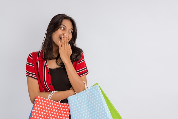 A beautiful asian girl closing her mouth while smiling with a lot of shopping bags at her hands on i