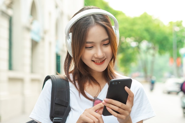 La bella ragazza asiatica sta usando il suo telefono per ascoltare la musica