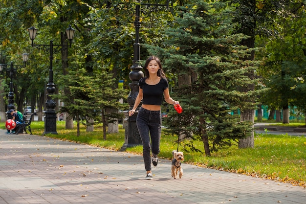 彼女の犬ヨークシャーテリアと夏に公園でジョギングする美しいアジアの女の子