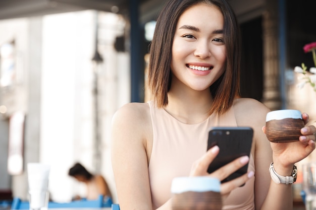 Beautiful asian girl resting in a cafe. Drinking tea and using mobile phone