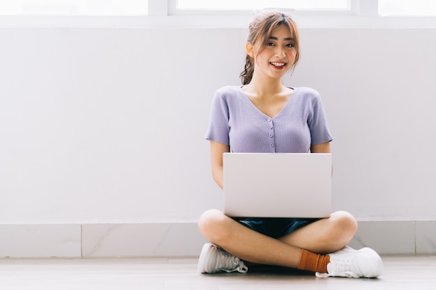 Bella ragazza asiatica che si siede sul pavimento e utilizzando il computer portatile a casa