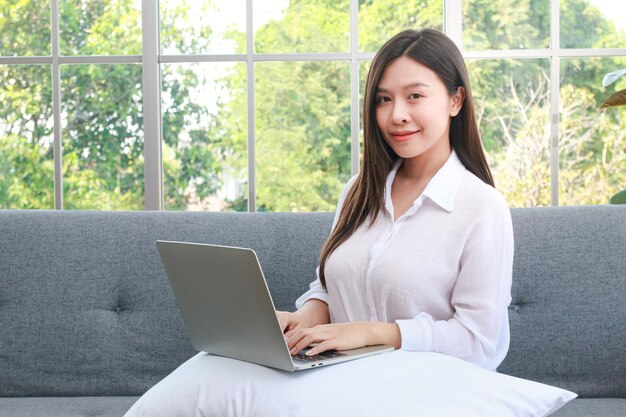 Beautiful asian girl Sitting on the sofa in the living room of the house. Work from home concept, freelance