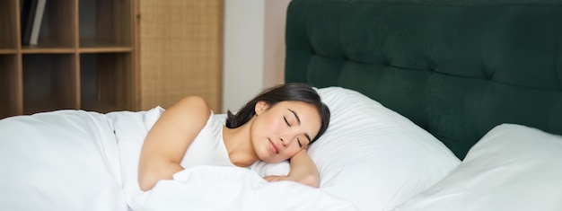 Photo beautiful asian girl sleeps in her bed with white sheets warm winter duvet smiling in her sleep