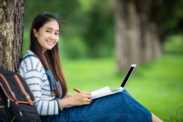 I bei libri asiatici della tenuta della studentessa e sorridere e l'apprendimento e il concetto di istruzione sul parco di estate per si rilassano il tempo