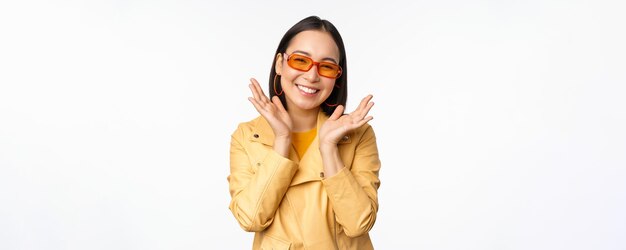 Beautiful asian girl in stylish sunglasses smiling happy looking bright and carefree standing over white background person