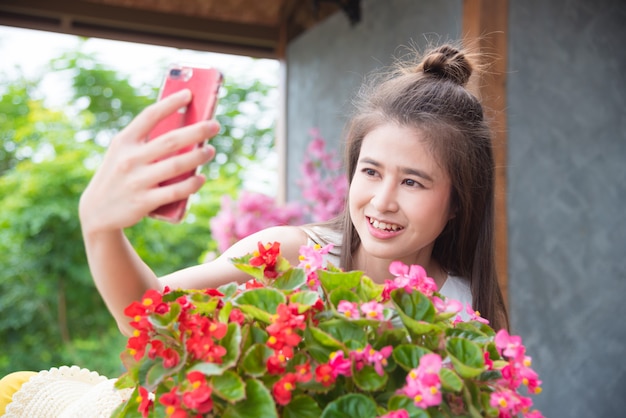 Beautiful asian girl taking her photo with flowers by smart phone