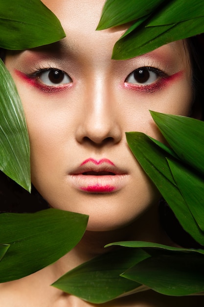 Beautiful Asian girl with a bright make-up art in green leaves.