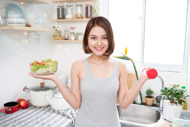 Beautiful Asian healthy girl with dumbbell and salad