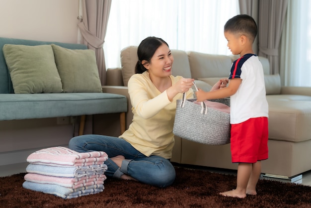 Beautiful Asian mother and child boy little helper are having fun and smiling while doing help her mother folded clothes laundry at home. Happy family.