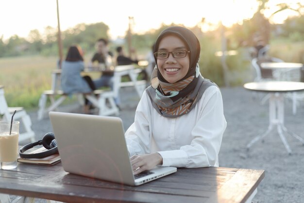 Красивая азиатская мусульманка в повседневной одежде работает с ноутбуком