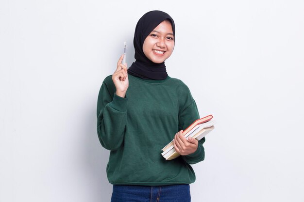 красивая азиатская мусульманка обнимает книгу кулаком и поднимает руку вверх на белом фоне