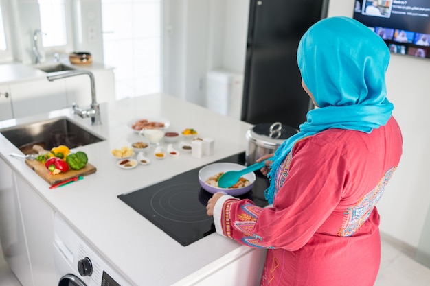 Beautiful asian muslim woman smile while looking to the camera in the kitchen isolated white background