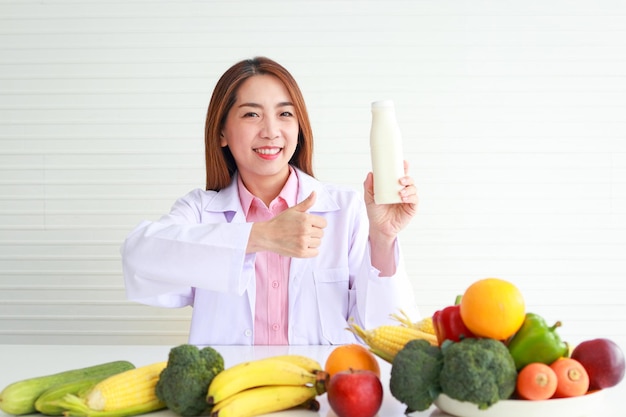 A beautiful Asian nutritionist sits at her desk holding a feeding bottle with fruits and vegetables she gave advice and prepare nutritious food Eat clean healthy food health care concept