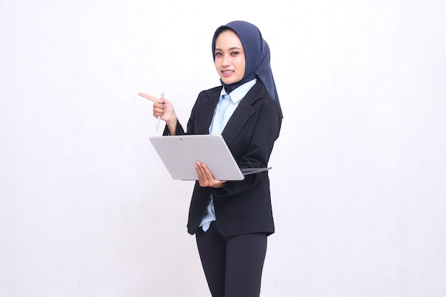 Beautiful Asian office woman wearing a hijab stands cheerfully at the camera gesturing right and ope