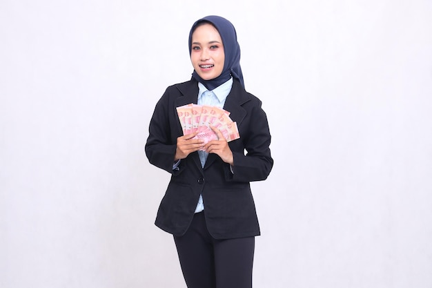 A beautiful Asian office woman wearing a hijab stands happily earning and bringing in rupiah from bu