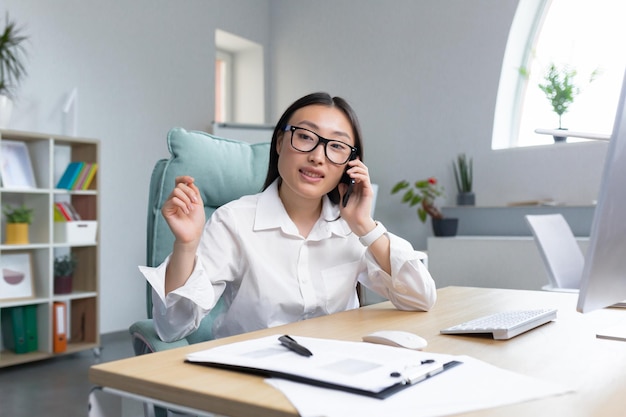 Beautiful asian office worker secretary working in modern office talking on the phone smiling and