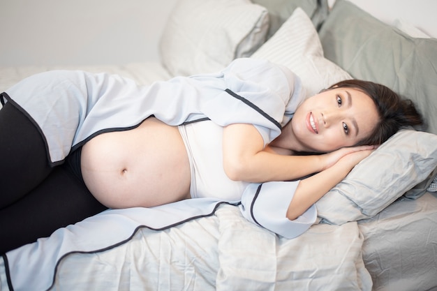 아름 다운 아시아 임신 한 여자는 침대에서 자
