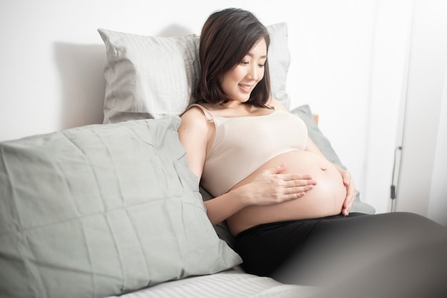 Красивая азиатская беременная женщина лежа на ее кровати