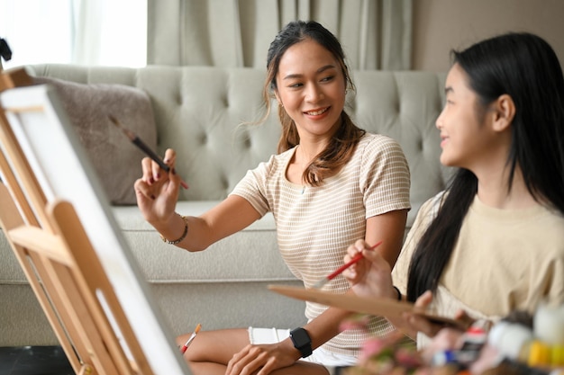 Beautiful Asian sister teaching her younger sister to paint an acrylic colour on canvas