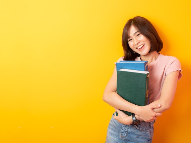 Bello studente asiatico felice sulla parete gialla