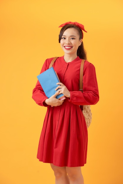 Beautiful Asian student holding books and bringing bag over orange background