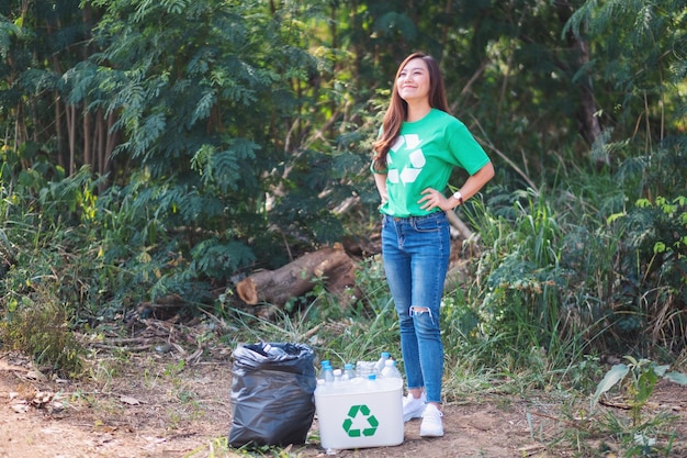 A beautiful asian woman activist finish collecting garbage  plastic bottles into a recycle bin and bag in the outdoors