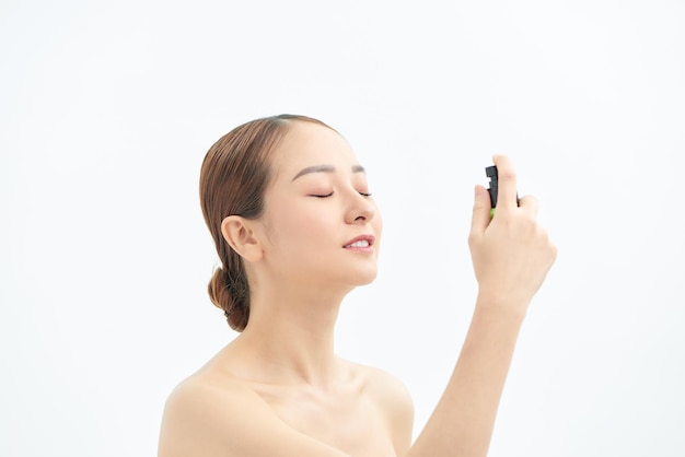 Beautiful Asian woman applying spray water on face on neutral background