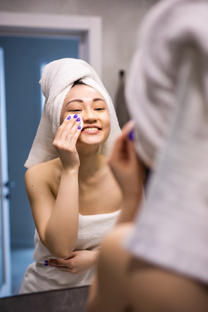 Beautiful asian woman bare skin in white bathrobe wash and\
clean facial with care in morning freshness sunlight