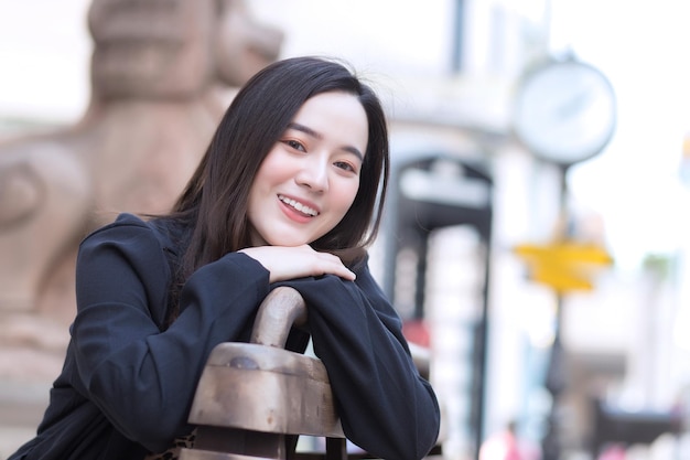 A beautiful Asian woman in a black long sleeve shirt sits happily on a chair in an outdoor park