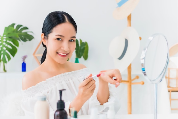 Beautiful asian woman blogger is showing how to make up and use cosmetics. In front of the mirror and camera recording vlog video live streaming at home.Skincare for healthy face concept.