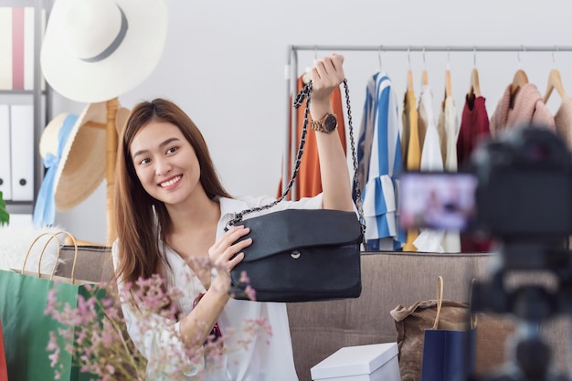 La bella blogger asiatica della donna sta mostrando e recensisce il prodotto. davanti alla telecamera per registrare video vlog in streaming live a casa. influenzatore online di affari sul concetto di social media.