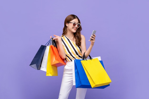 Beautiful Asian woman carrying colorful bags shopping online with mobile phone