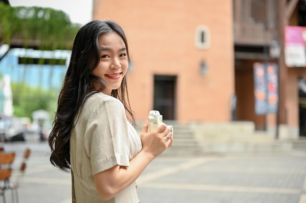 A beautiful Asian woman in casual clothes strolling around the city with her instant camera