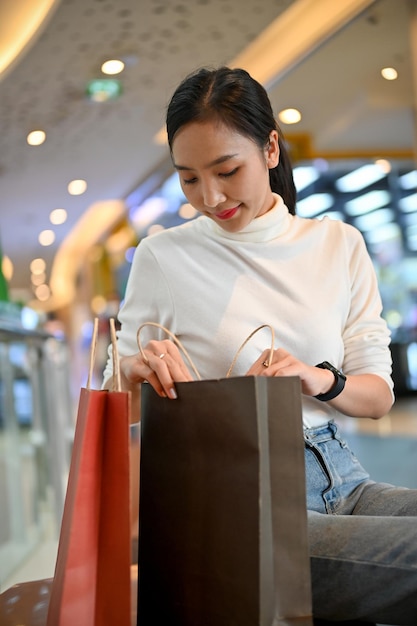 Beautiful Asian woman checking her purchased clothes while resting in the mall